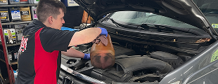 A man is holding a bag of oil under the hood of a car. | Ed's Automotive