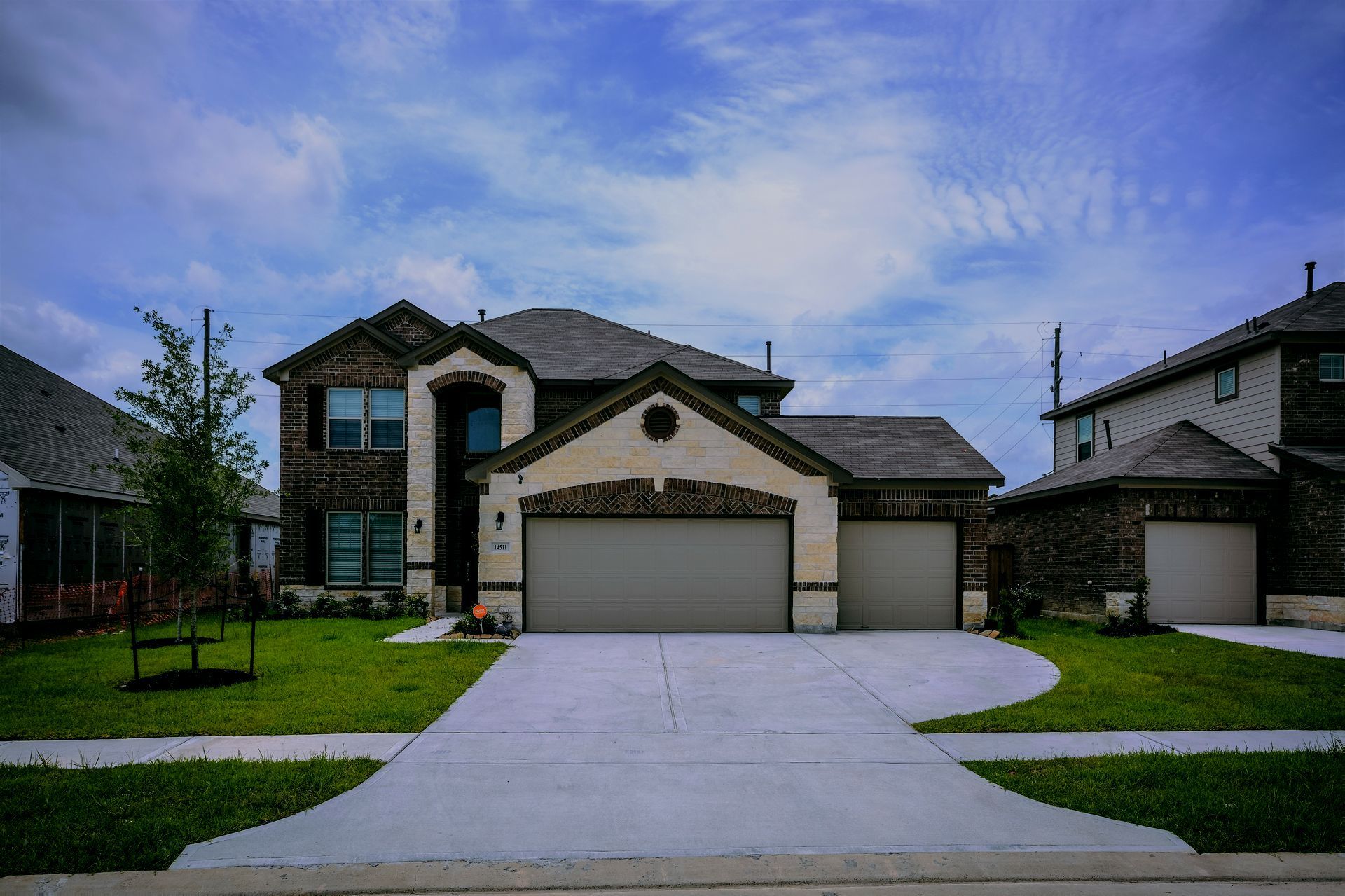 A large house with three garage doors is sitting on top of a lush green lawn.