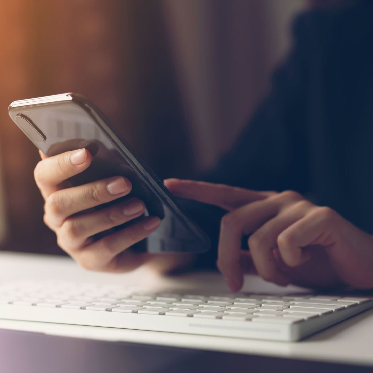 A person is holding a cell phone in their hand next to a keyboard.