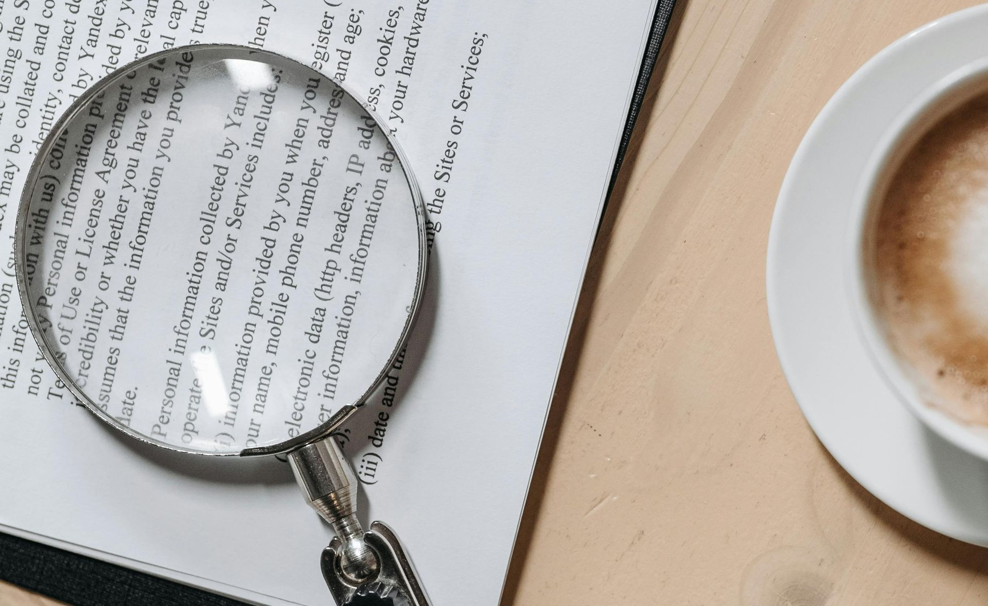 Magnifying glass on a document next to a cup of coffee, symbolising careful review