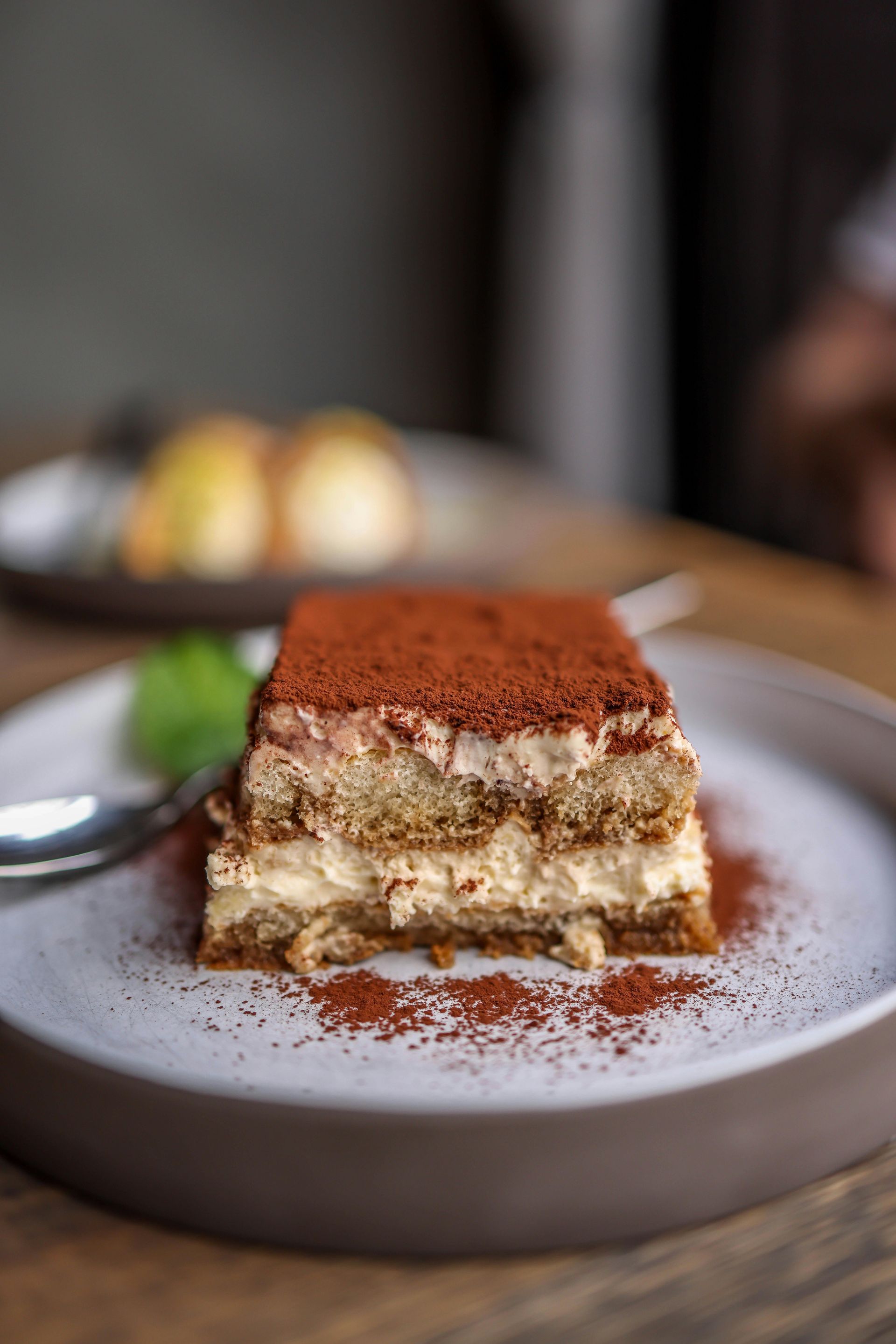 Tiramisu on a plate dusted with cocoa powder, garnished with mint.