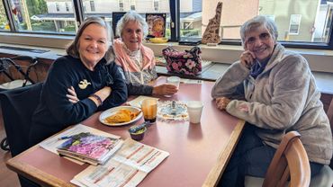 Three women seated at a table in a cafe, smiling and looking at the camera.