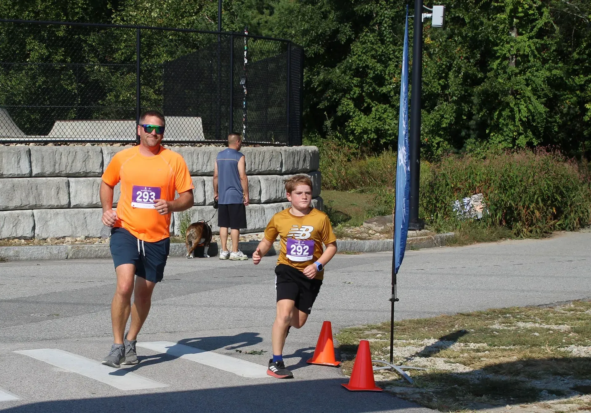 Man in orange shirt and boy in gold shirt running race. Outdoors on sunny day.