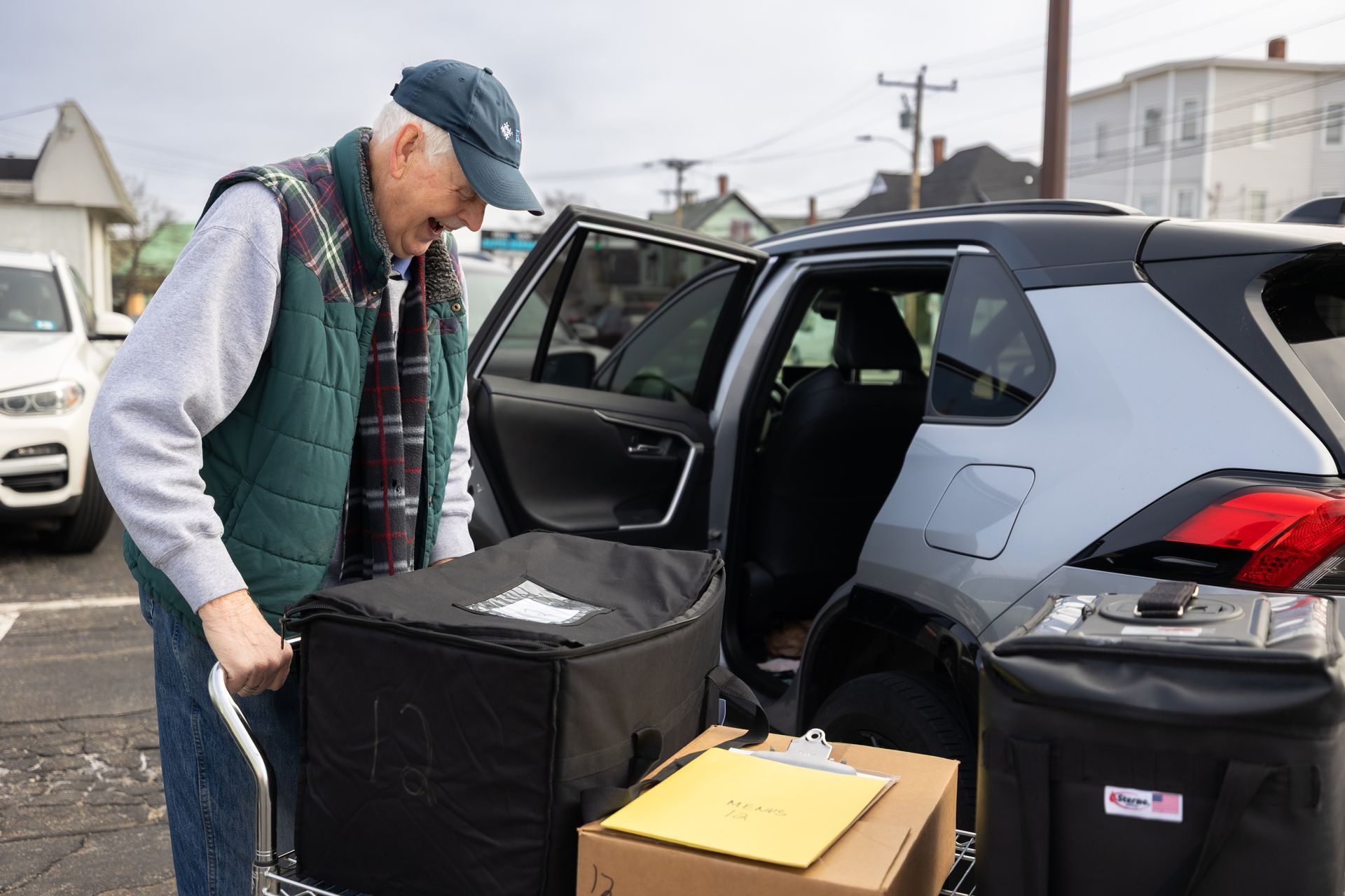 Three women in an interior space smile near windows. One wears a green top, others wear aprons.