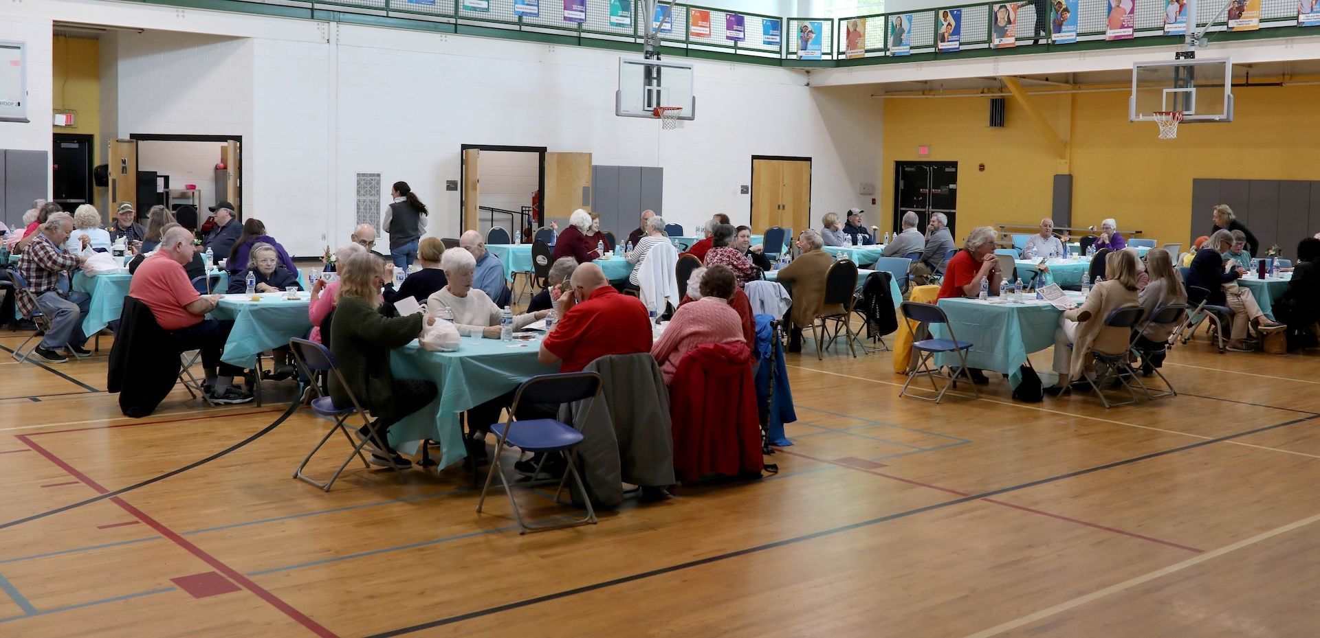 People seated at tables in a gymnasium, likely an event or gathering.