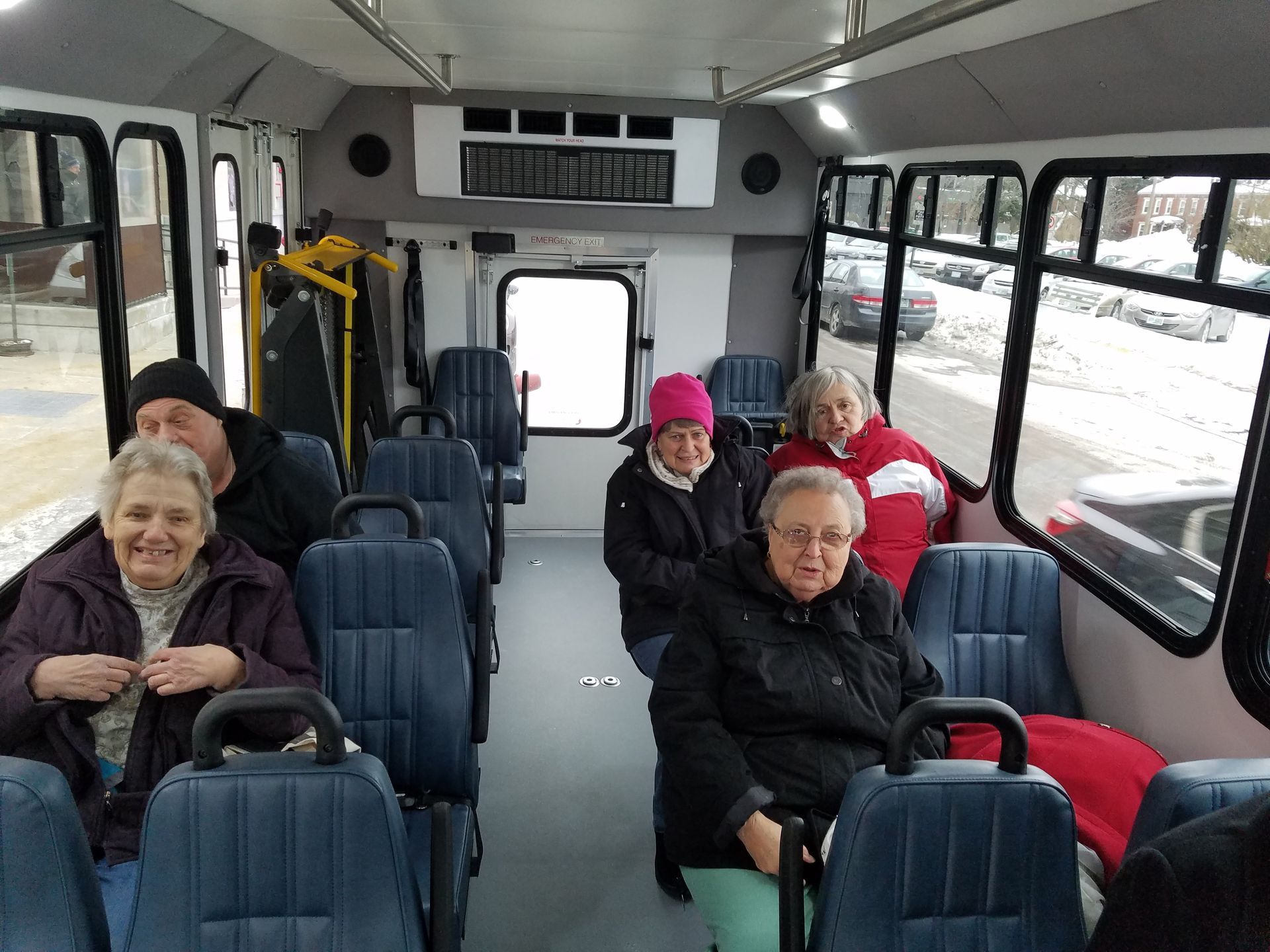 People inside a bus with blue seats, looking at the camera. Snowy scene visible through windows.