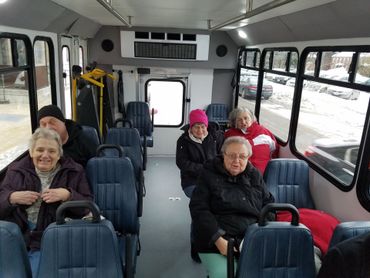 People inside a bus with blue seats, looking at the camera. Snowy scene visible through windows.