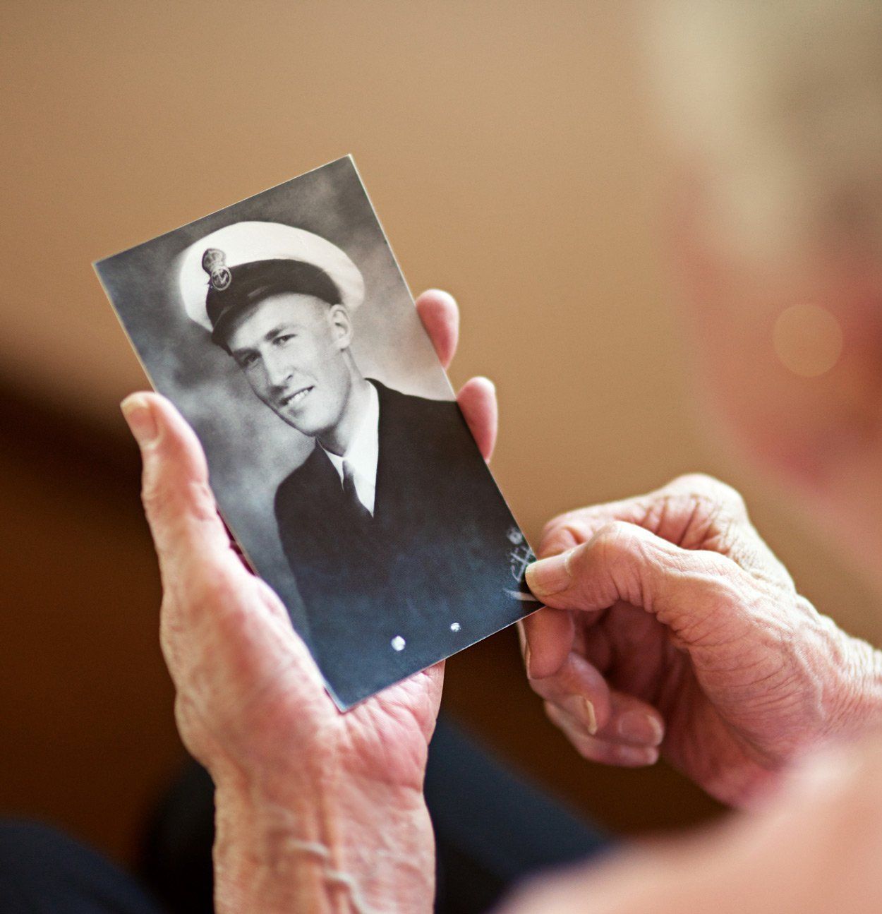 Elderly person holding a black and white photo of a man in a navy uniform.