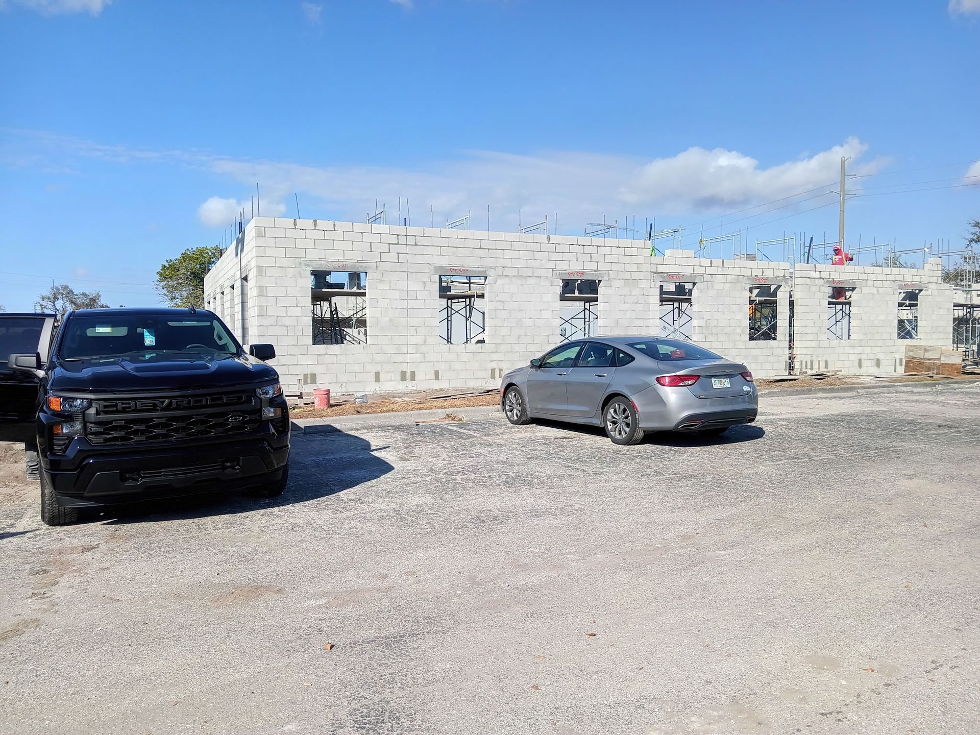 Black pickup truck and gray sedan parked in front of a building under construction.