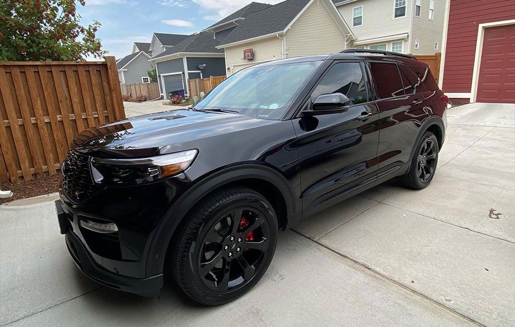 A black ford explorer is parked in a driveway in front of a house.