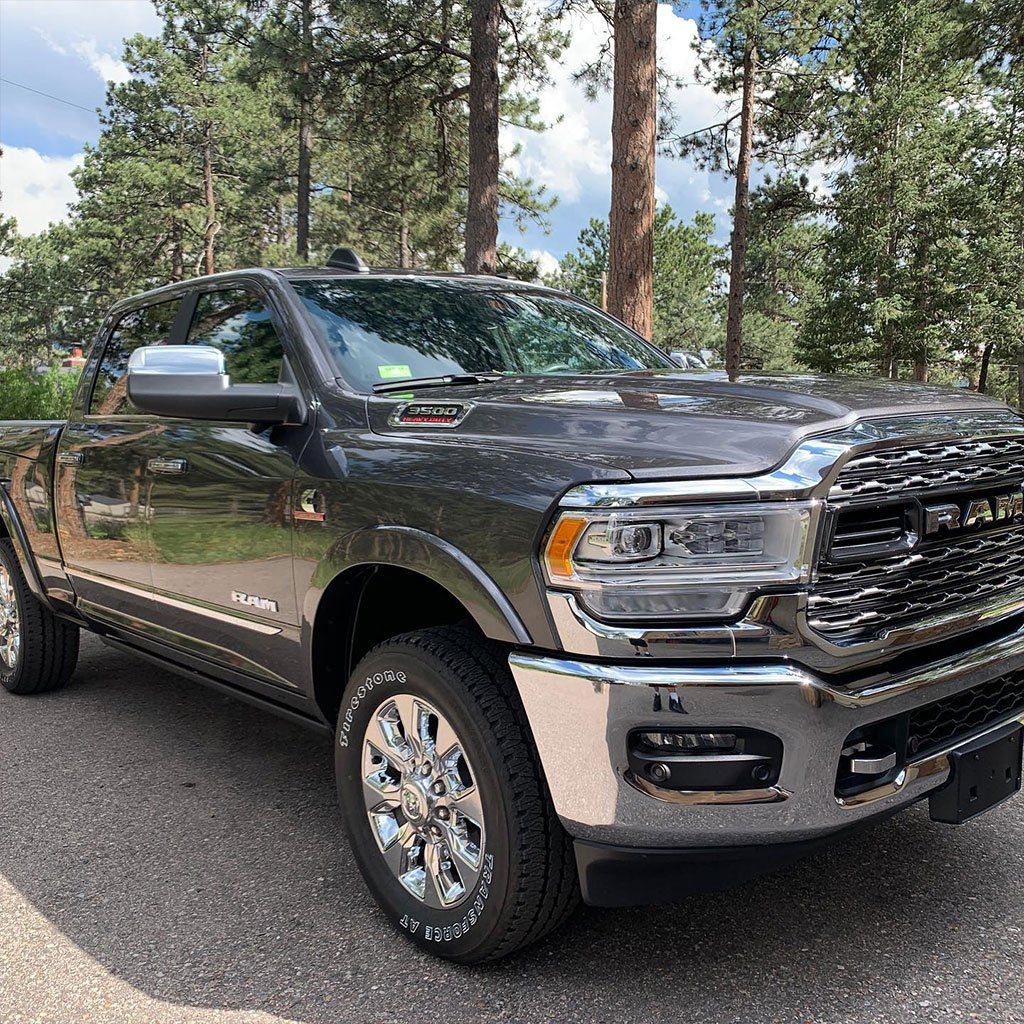 A black ram truck is parked on the side of the road in front of a forest.