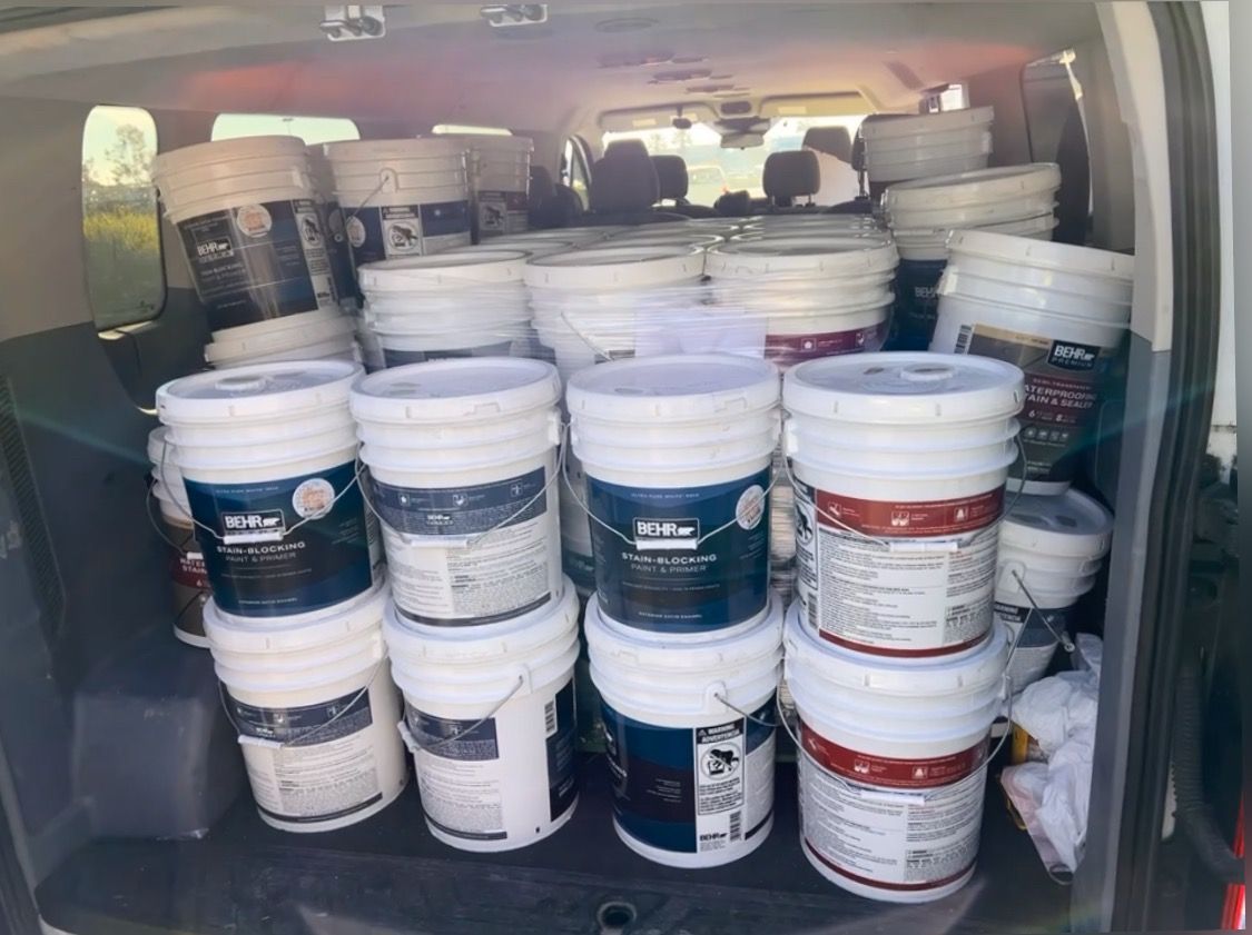 Buckets of paint are stacked in the back of a van.