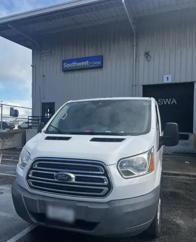 A white ford van is parked in front of a warehouse