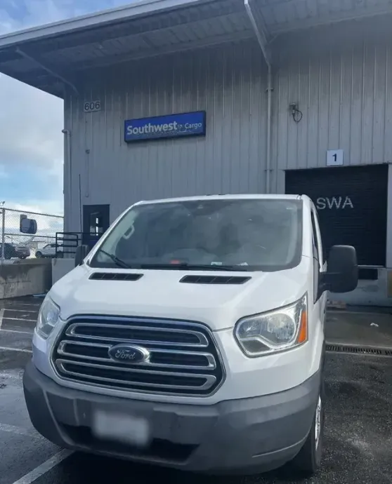 A white ford van is parked in front of a warehouse
