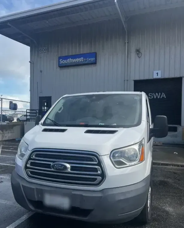 A white ford van is parked in front of a warehouse
