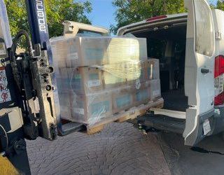 A white van is being loaded with boxes and pallets.
