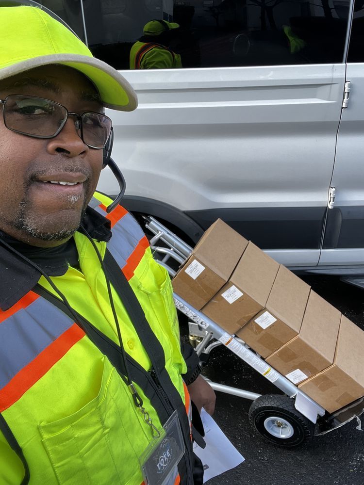 A man in a yellow vest is standing next to a cart with boxes on it.