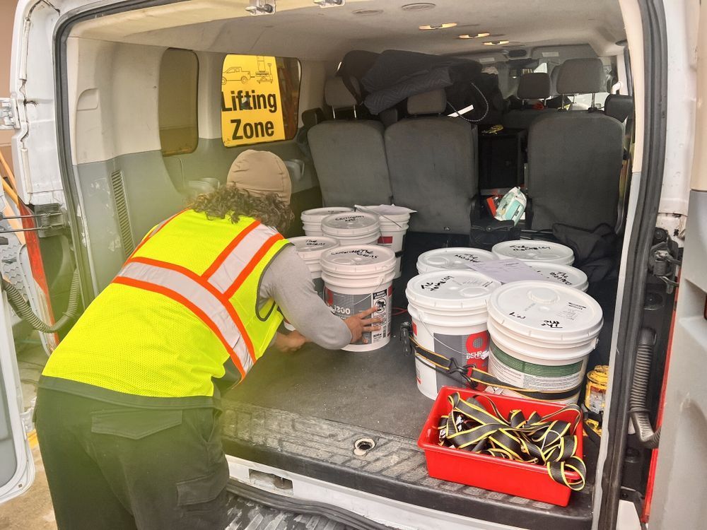 A man in a yellow vest is loading buckets into the back of a van.