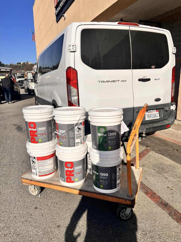 A white van is parked next to a cart filled with buckets of paint.