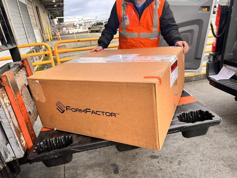 A man in an orange vest is holding a large cardboard box.