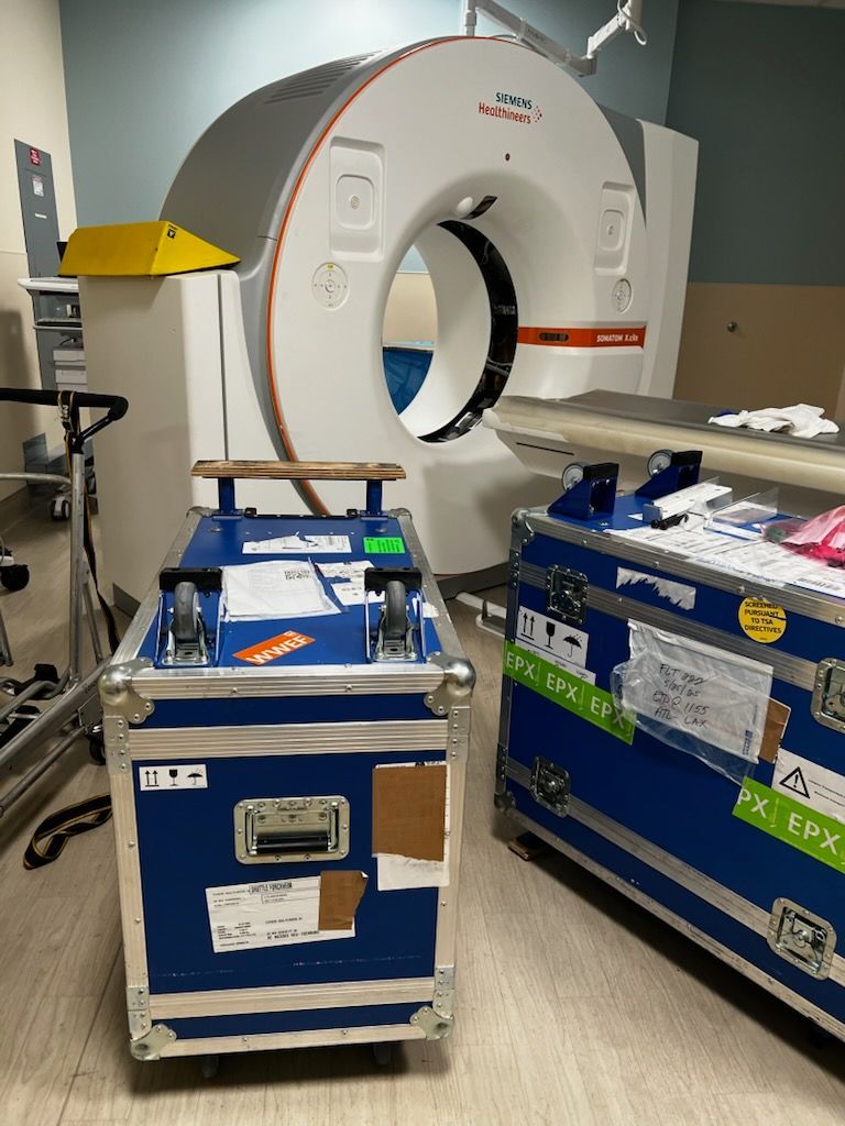 A ct scan machine is sitting in a room next to two blue cases.
