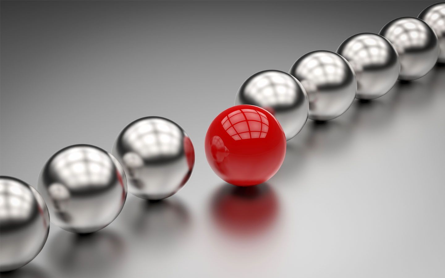 Red sphere among a line of silver spheres on a reflective gray surface.