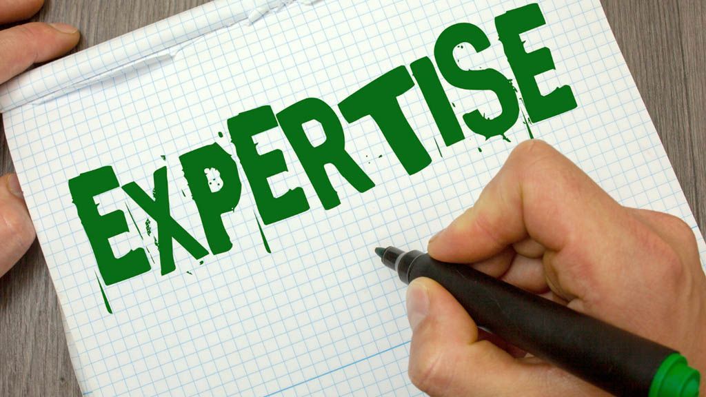 A person is writing the word expertise on a piece of paper.
