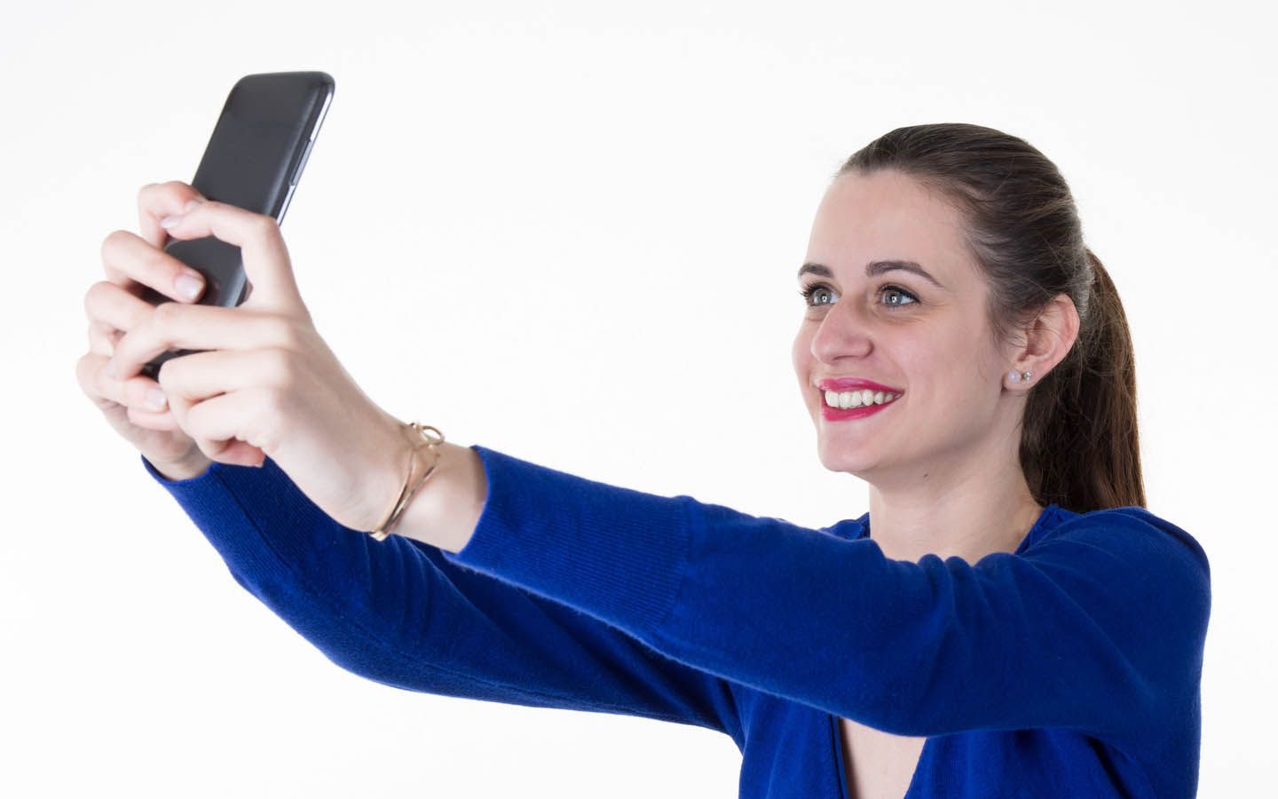 Woman in blue sweater taking a selfie with a smiling expression, against a white background.