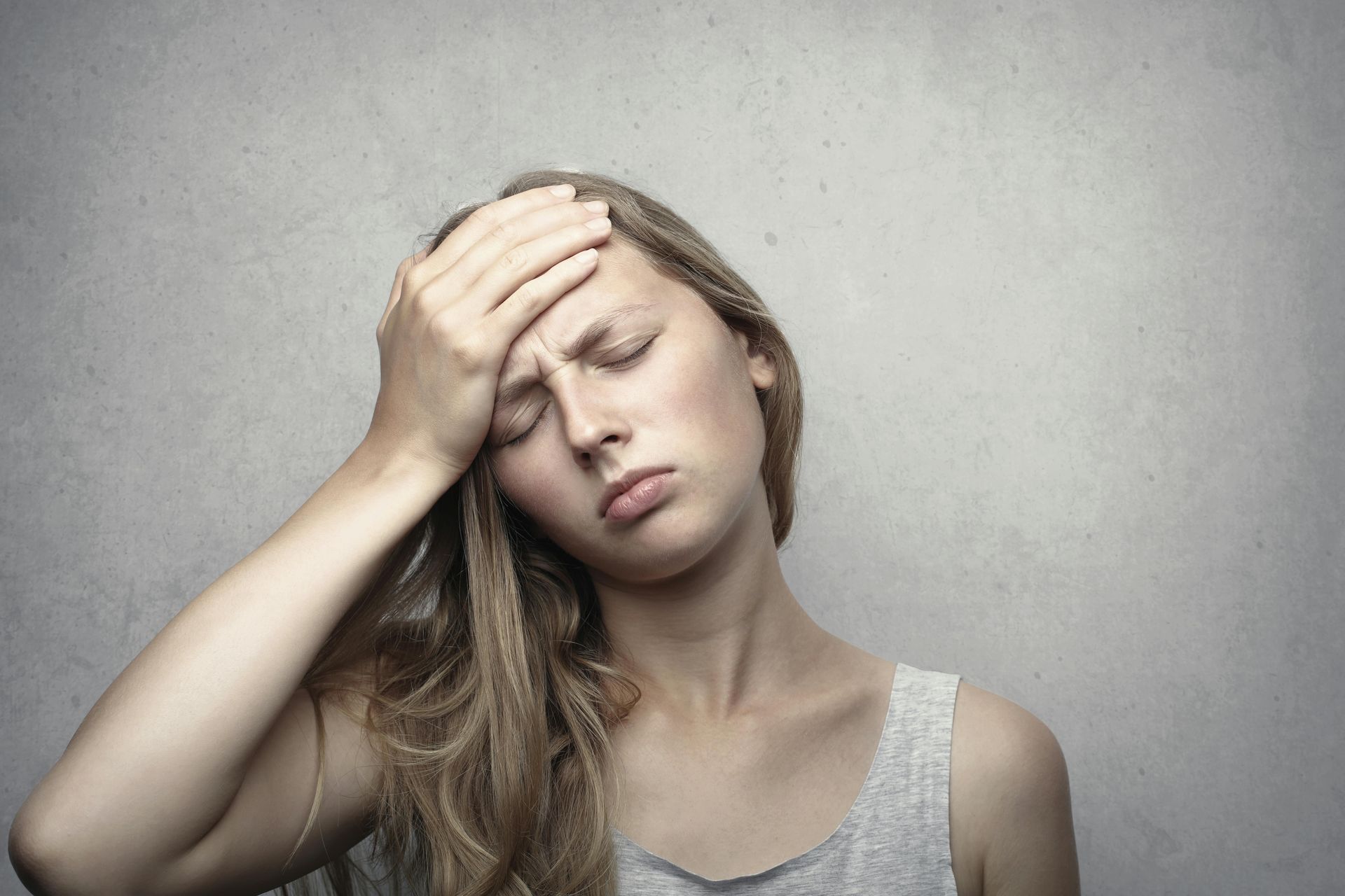 Vrouw met lang blond haar die haar rechterhand op haar voorhoofd legt. Ze ziet er ziek uit.