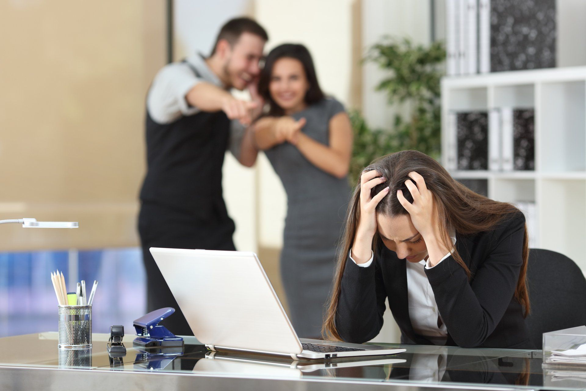 Twee zakenlieden pesten een trieste collega die zit op haar werkplek op kantoor