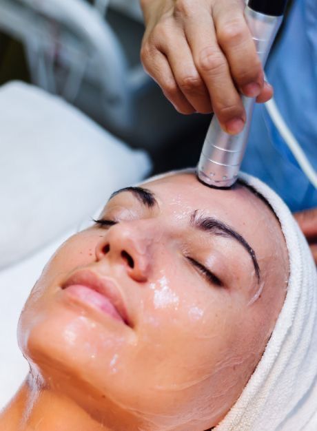 Facial treatment with a handheld device applied to a woman’s forehead in a spa setting