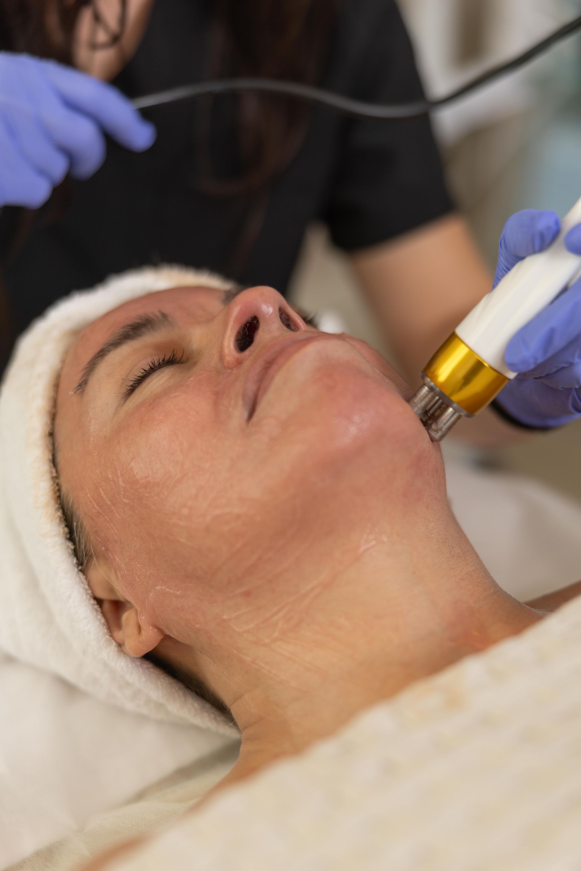 A facial treatment with a handheld device on a reclining client, wearing gloves in a spa setting.