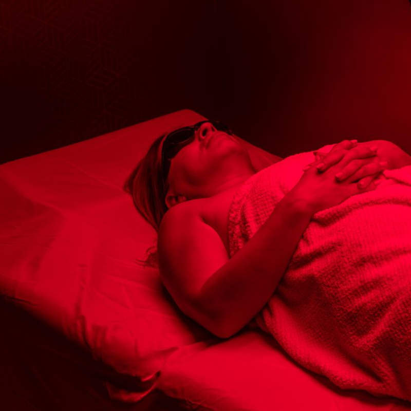 Person lying in bed under a blanket, lit by intense red light.