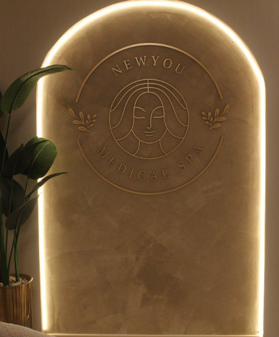 Warmly lit arched wall with engraved logo and text, beside a leafy potted plant