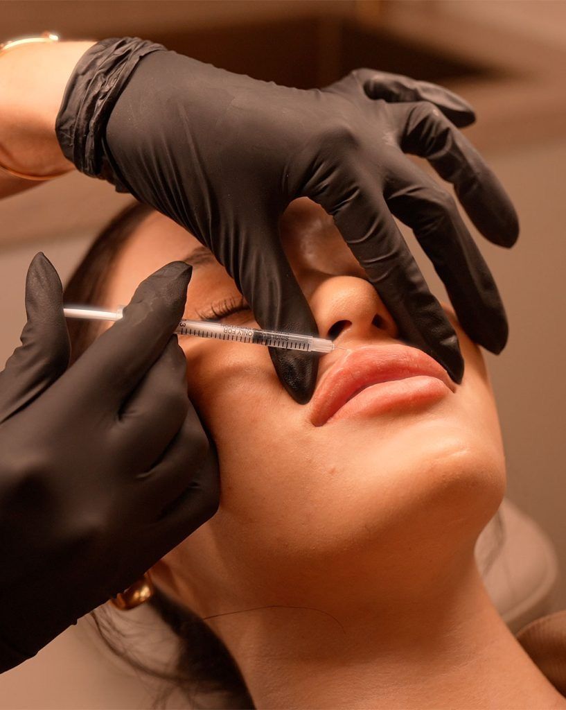 Gloved hands measure a womanβs nose with calipers during a cosmetic consultation