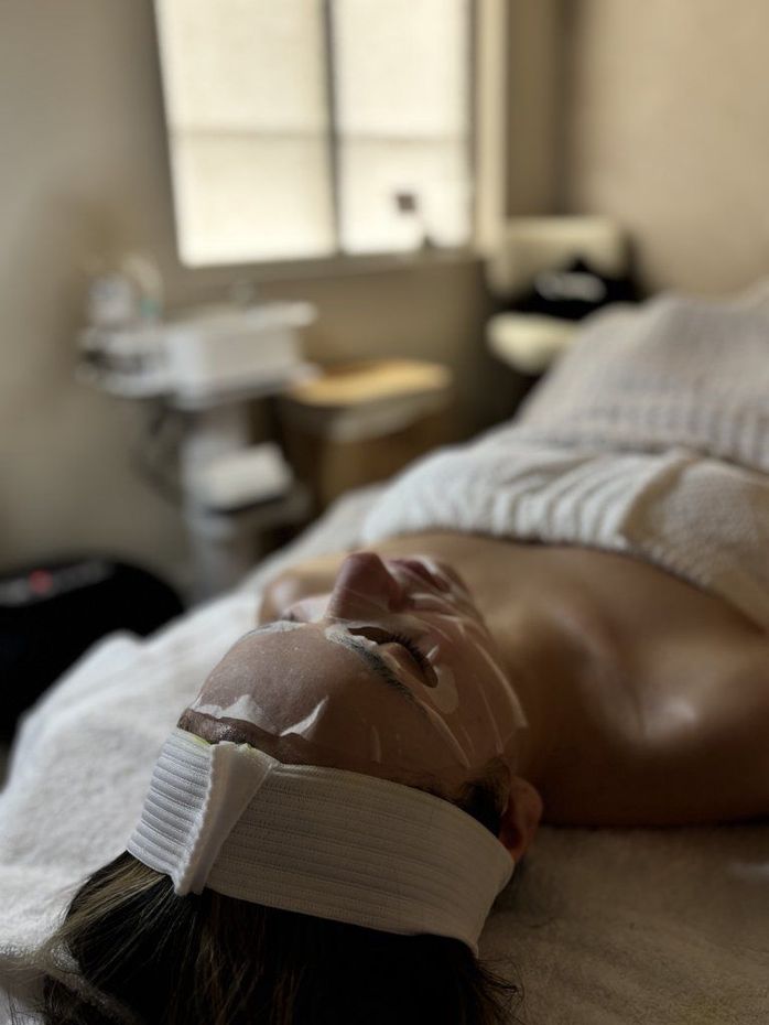 Person lying on a massage table with facial treatment strips in a spa room