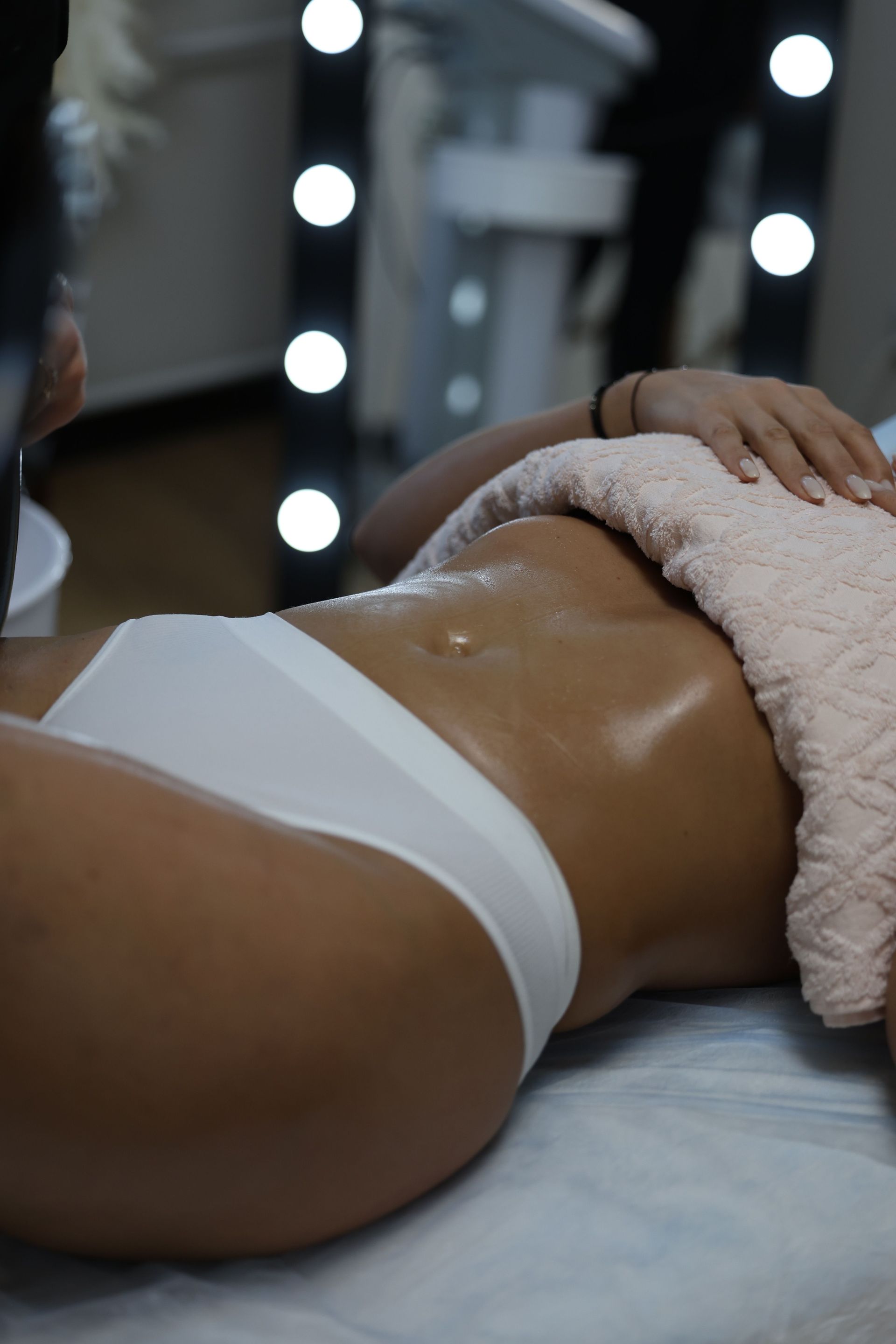 Person lying face down on a treatment table during a massage, wearing white underwear and a pink towel.