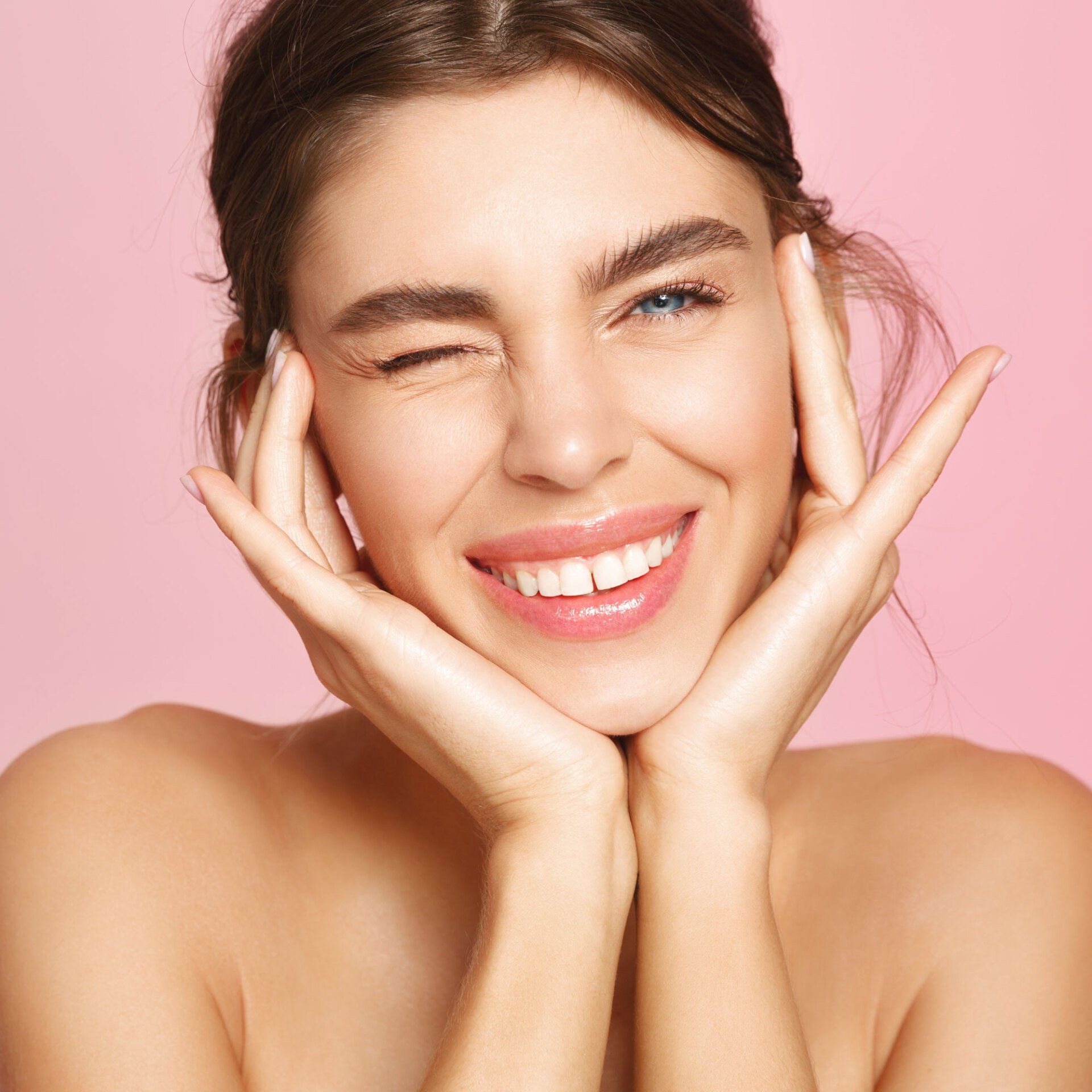 Young woman winking and smiling while holding her face