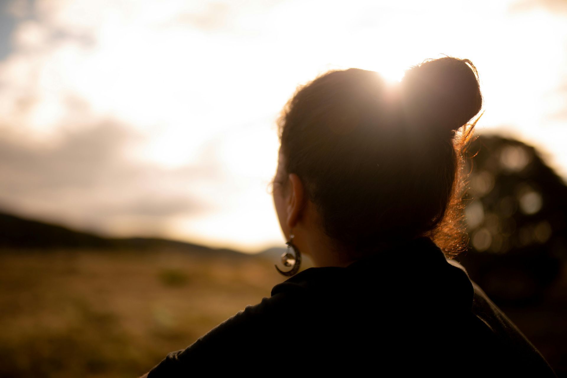 Woman looking toward the sunlit horizon, outdoors, bun hairstyle, silhouette.