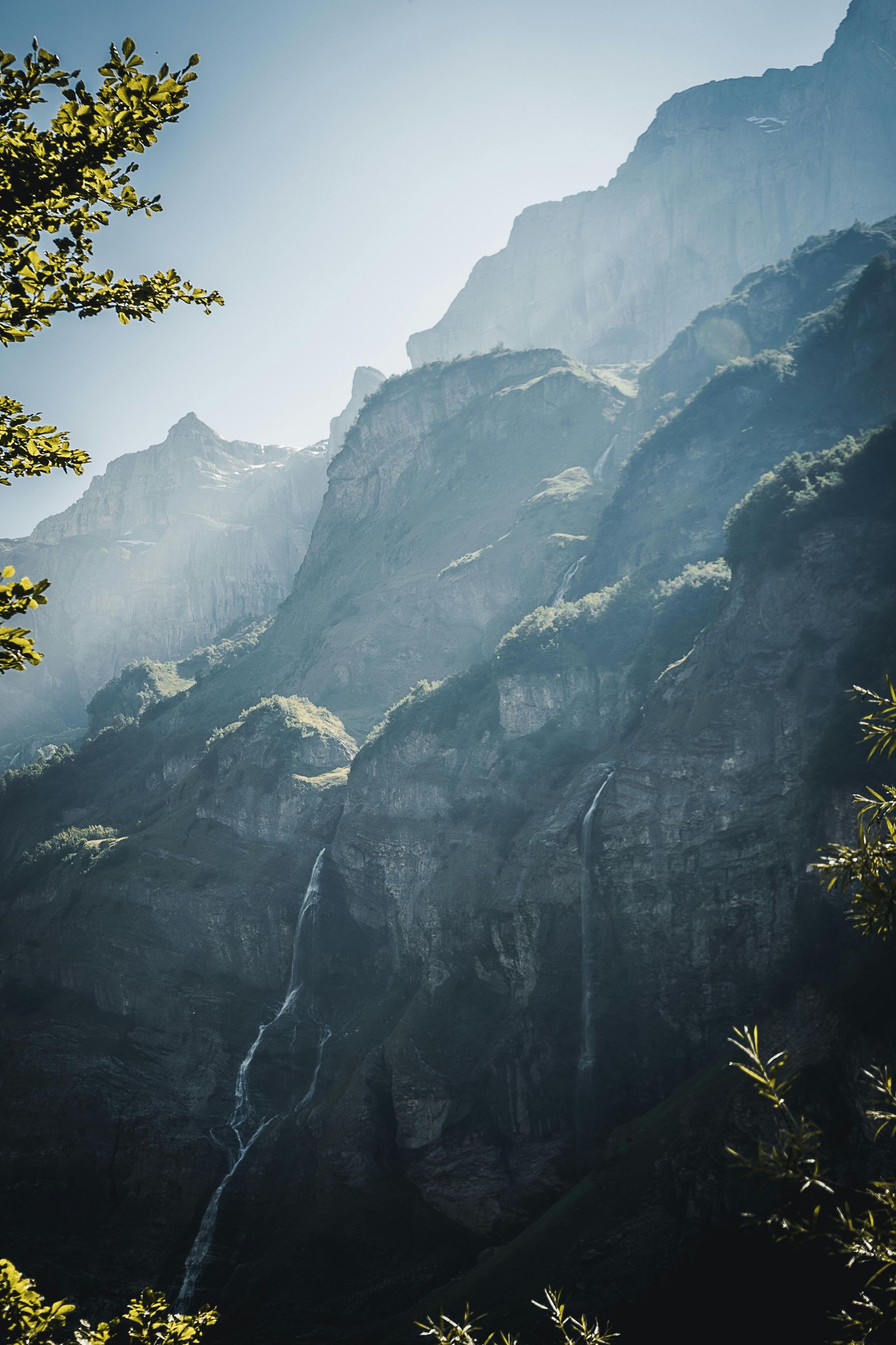 Sunlit mountain range with a waterfall cascading down a rocky cliff.