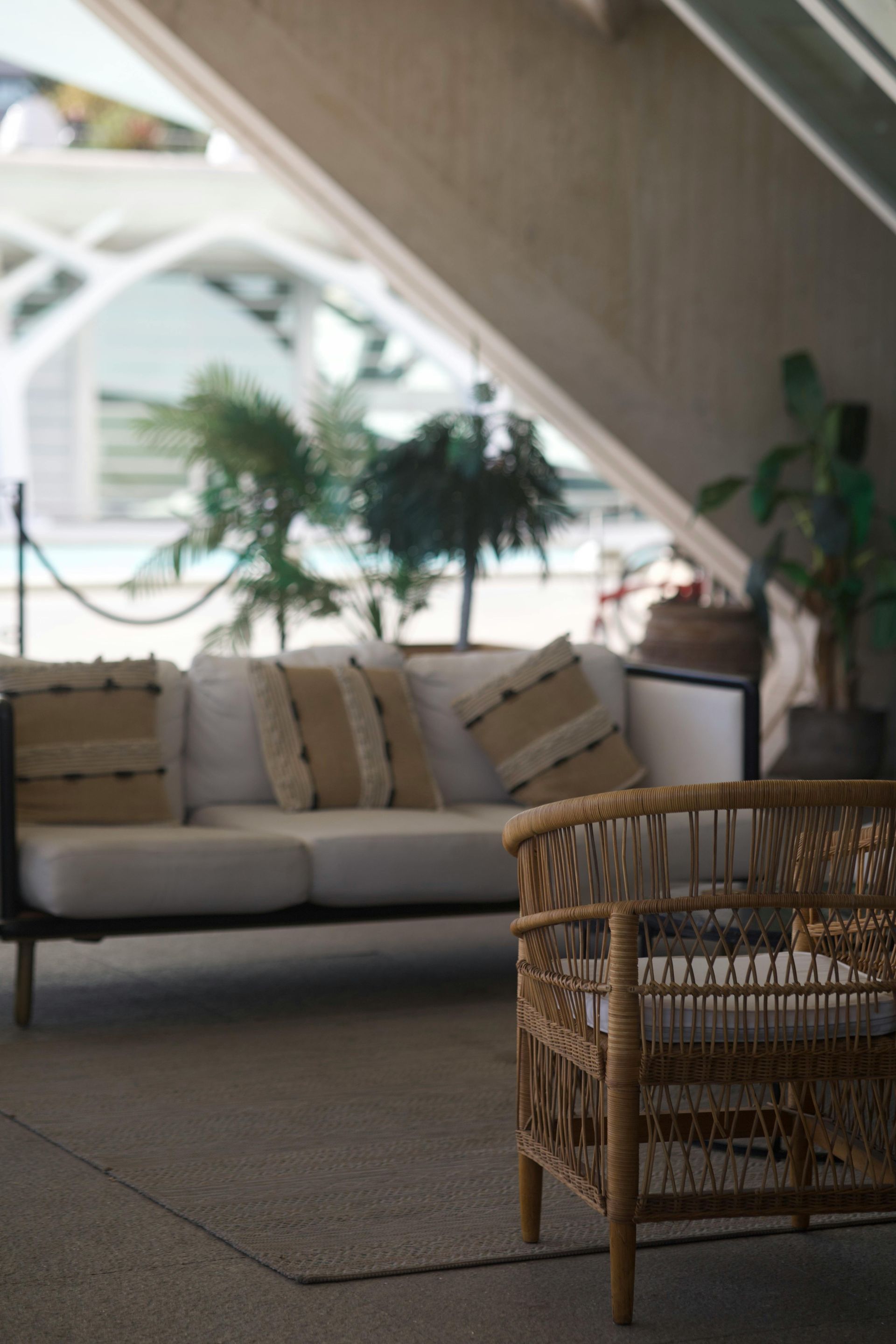 Outdoor seating area with white sofa, rattan chair, plants, and architectural details in background.