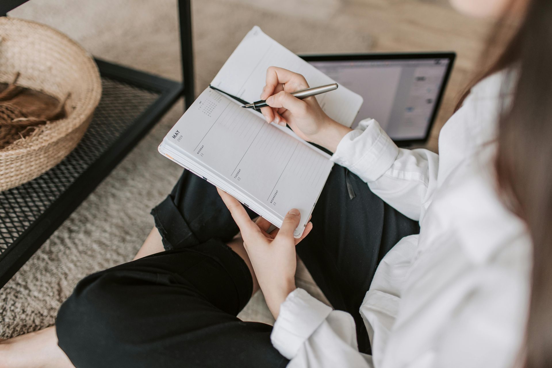 Woman sitting on the floor writing in a notebook, laptop open nearby.