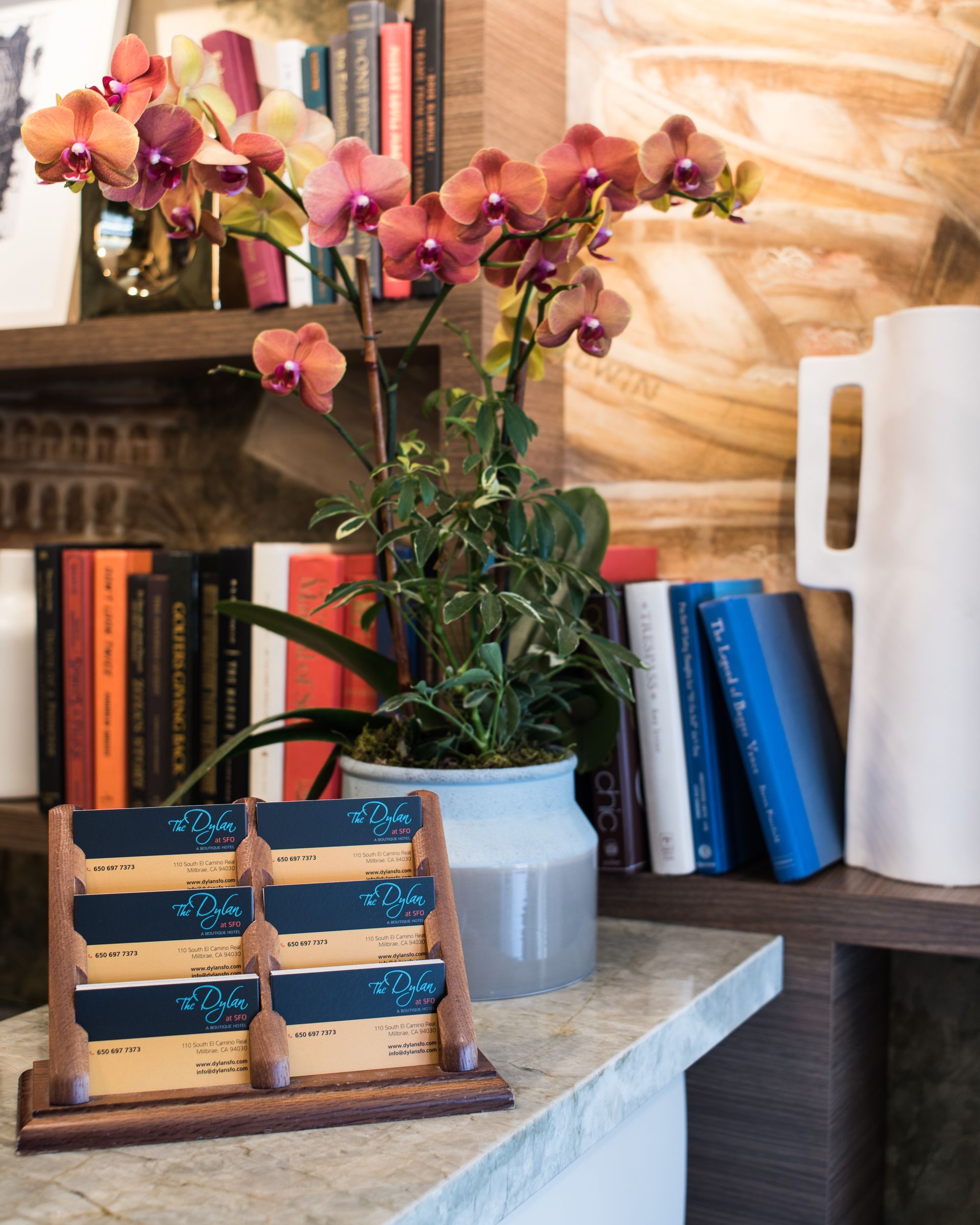 A wooden rack displaying business cards sits on a stone counter next to an orchid plant and bookshelves.