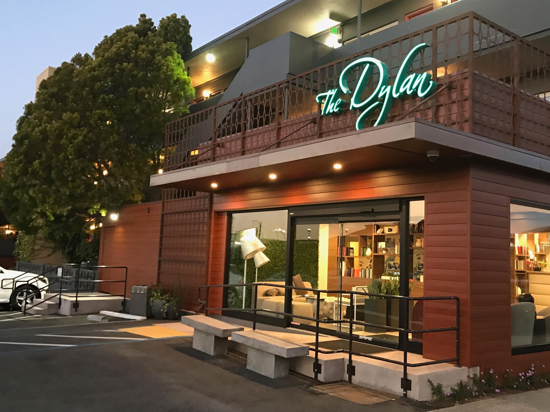 The exterior of The Dylan, a modern building with wood paneling, a large glass entrance, and a balcony at dusk.