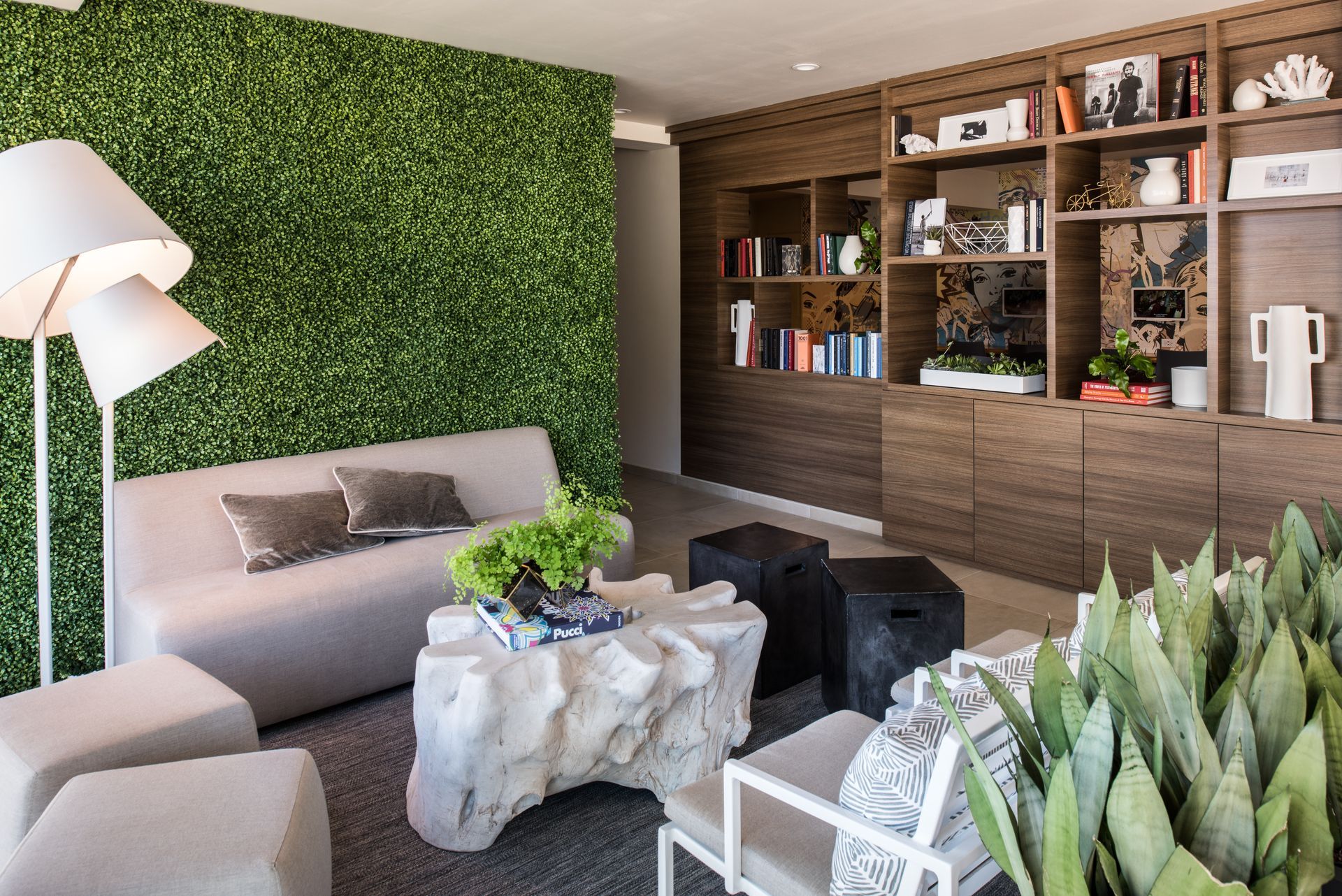 A lounge area features a sofa, a white carved wood coffee table, two cube stools, a green wall, and a large wood bookshelf.