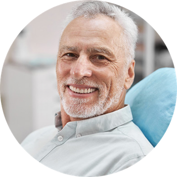 A man with a beard is smiling while sitting in a dental chair.