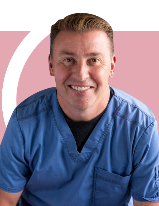 A man in a blue scrub is smiling in front of a pink background