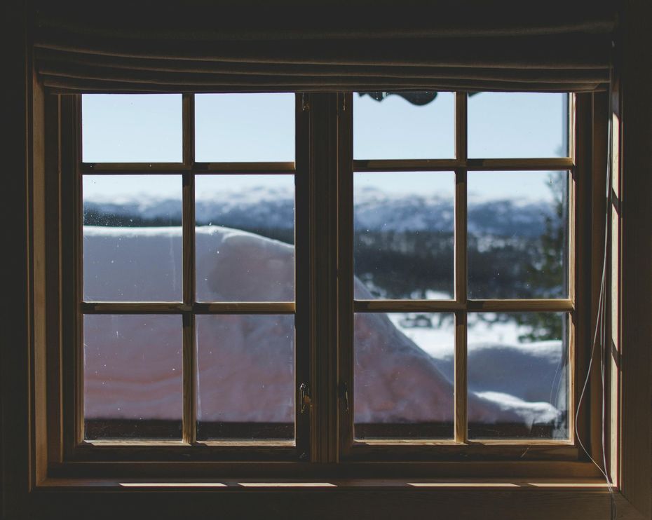 Wooden window with grid panes looking out at snow-covered landscape and blue sky.