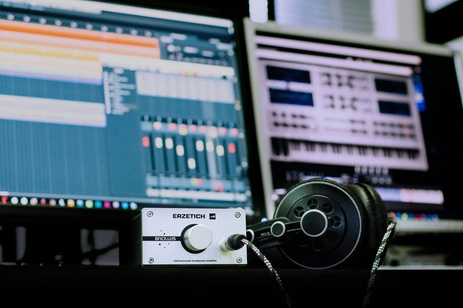 Audio mixing desk with headphones in front of dual computer monitors showing music production software