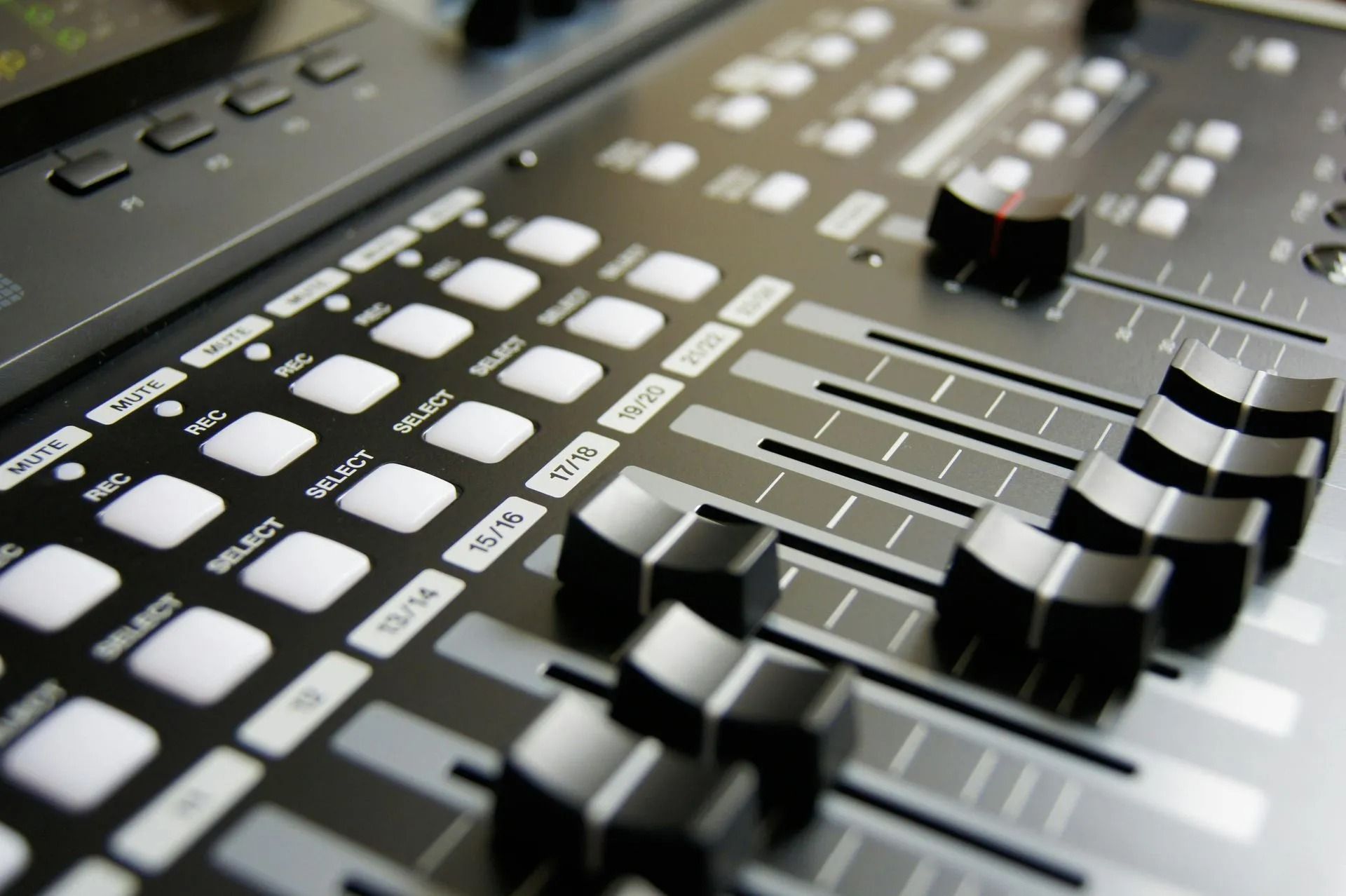 Close-up of a black audio mixing console with white buttons and sliding faders
